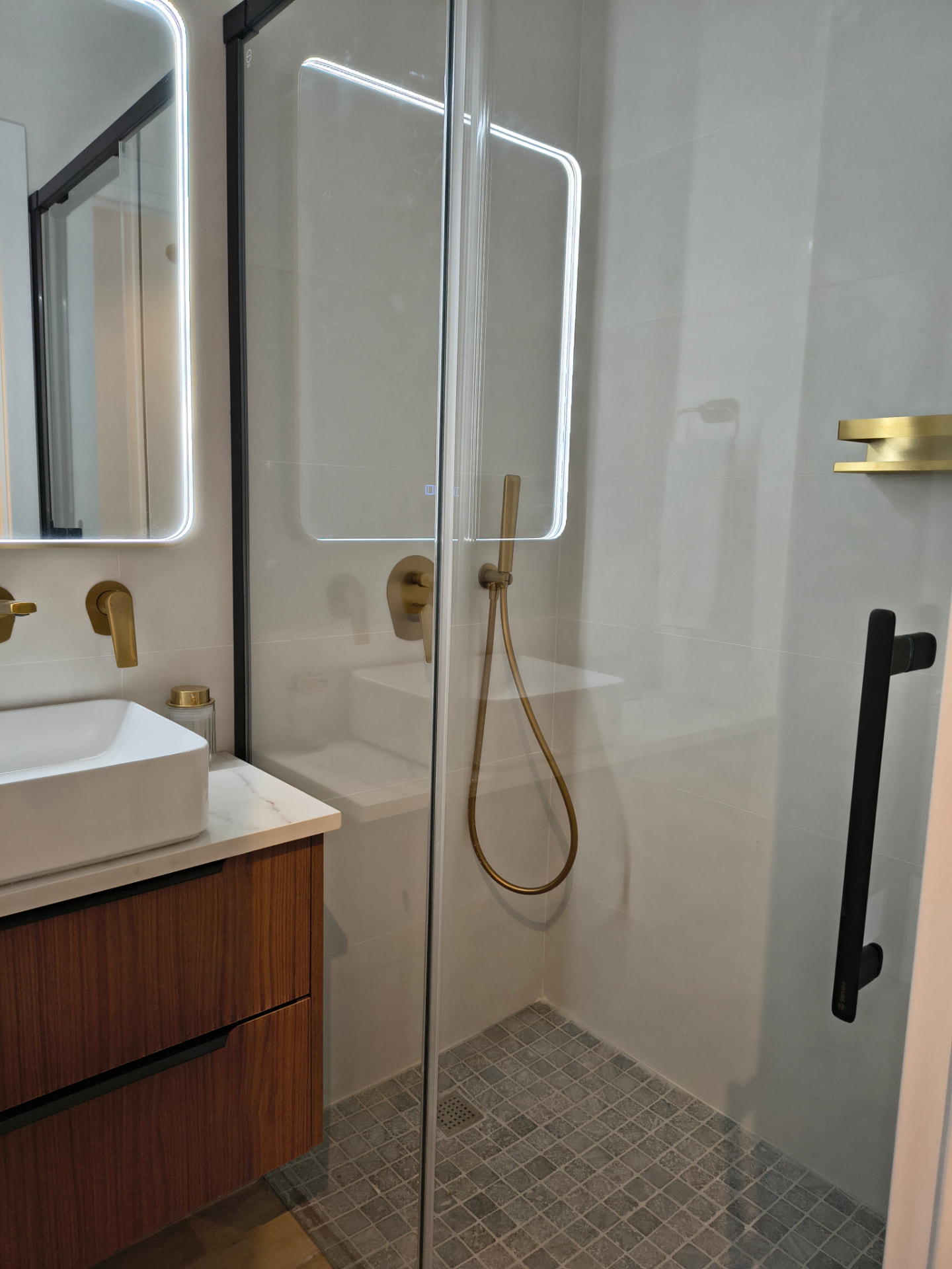 Bad mit gemauerter Dusche, schwarzer Duschabtrennung, goldenen Armaturen und Nussbaummöbel