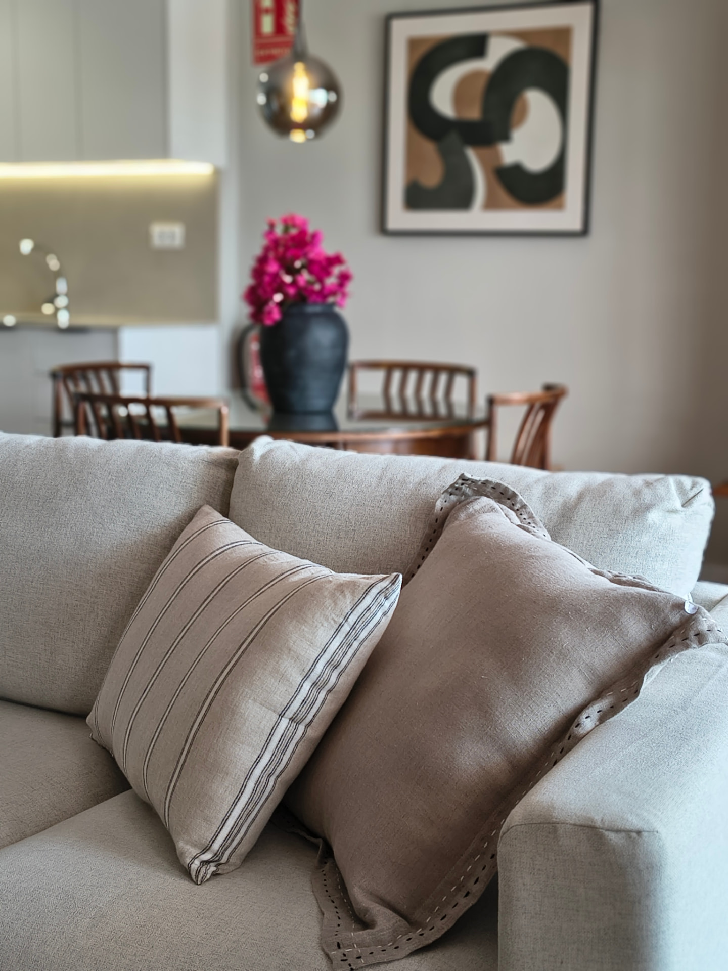 Detail eines Leinensofas mit gestreiften Kissen und Essbereich im Hintergrund