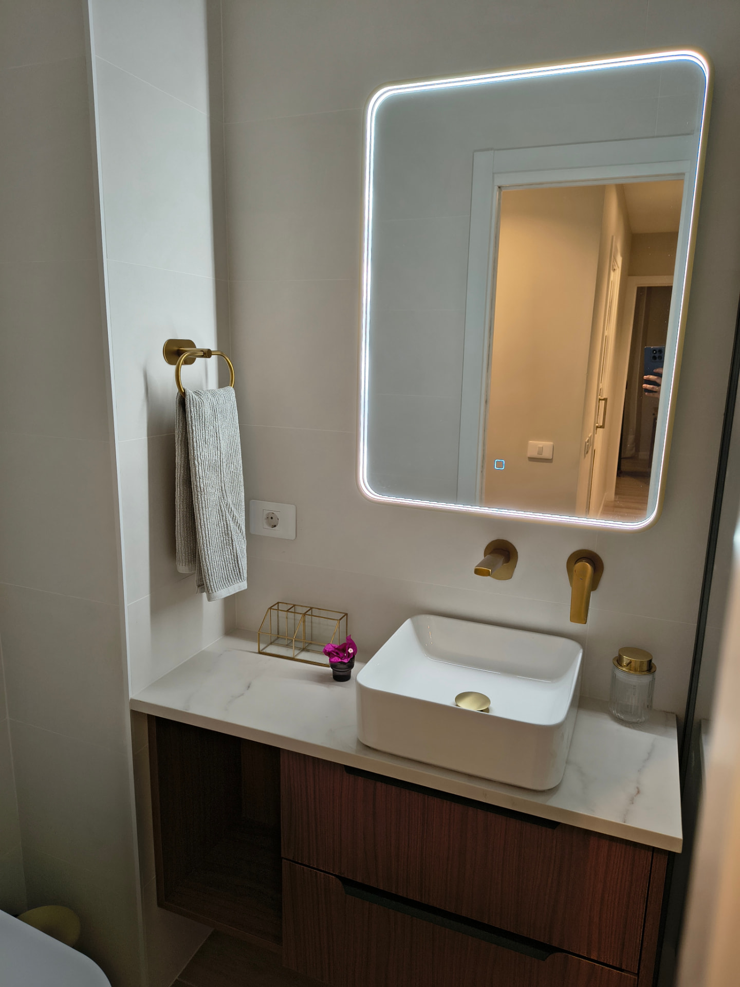 Waschbecken auf marmorierter Arbeitsplatte mit hinterleuchtetem Spiegel und goldenen Armaturen