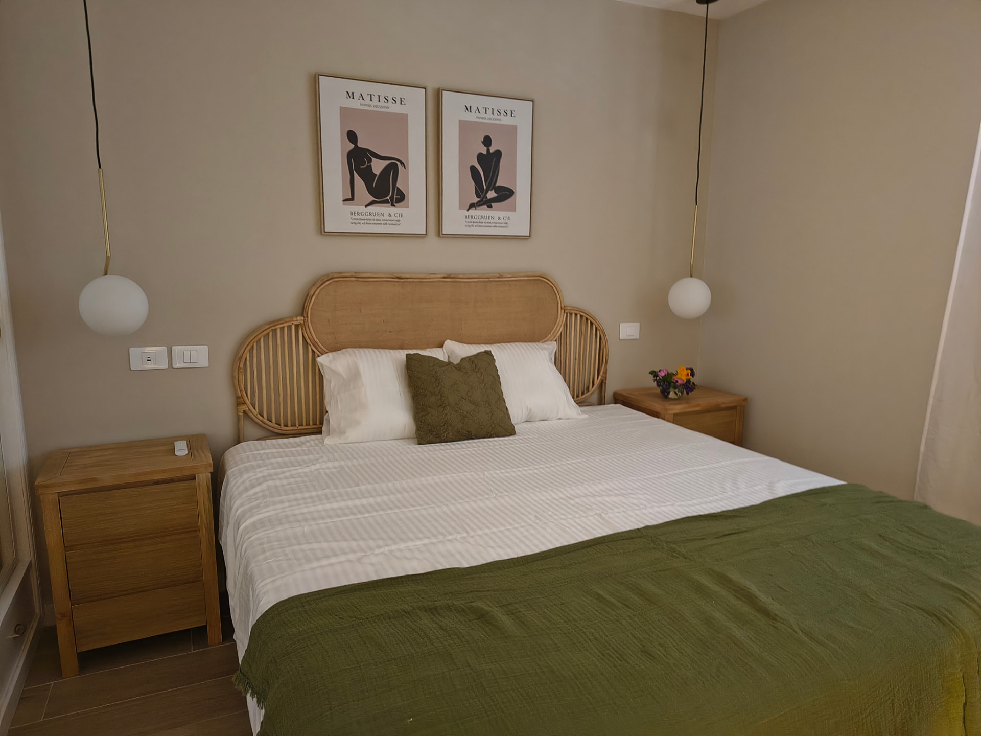 Schlafzimmer mit Rattan-Kopfteil, Holznachttischen und olivgrüner Tagesdecke