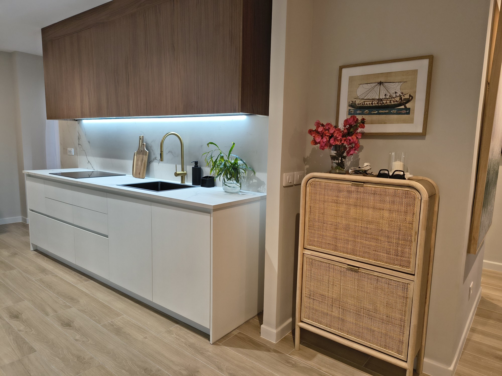 Weiße Küche mit goldenen Armaturen und Beistellmöbel aus Rattan