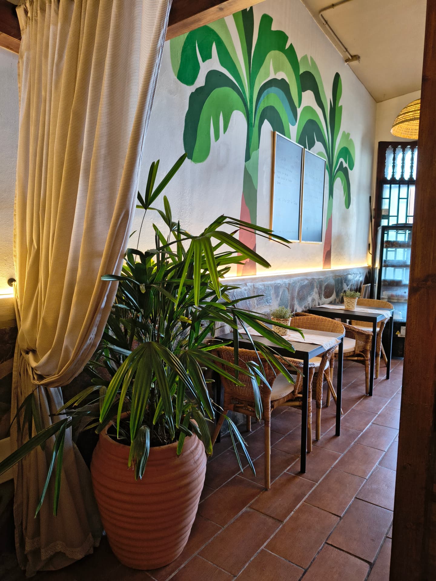 Restaurant-Essbereich mit Wandbild aus Bananenstauden, Faserstühlen und Lehmboden