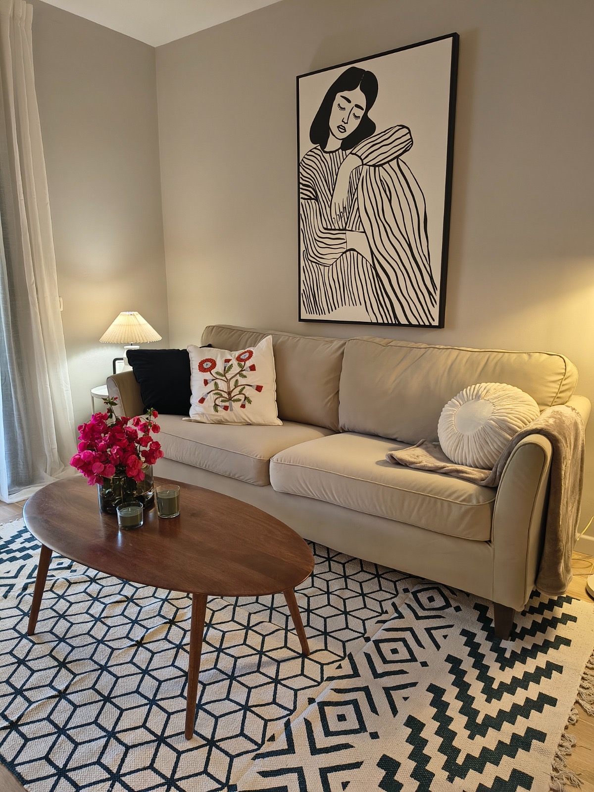Renoviertes Wohnzimmer mit beigefarbenem Sofa, geometrischem Teppich und gerahmtem Kunstdruck